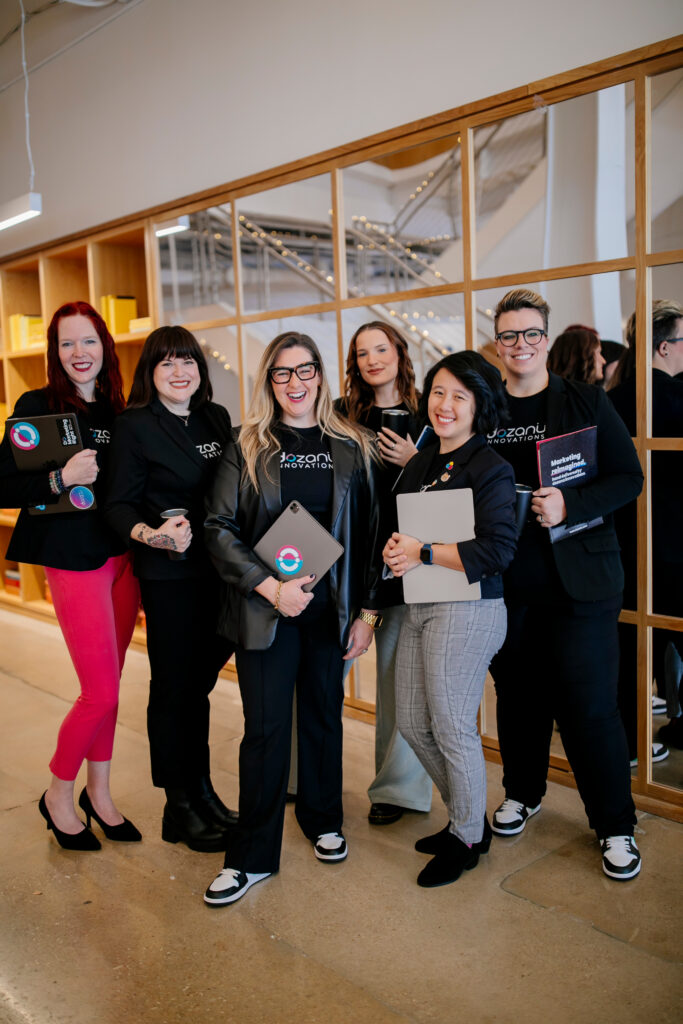 The dozanü team standing together in a hallway holding their laptops and notebooks.