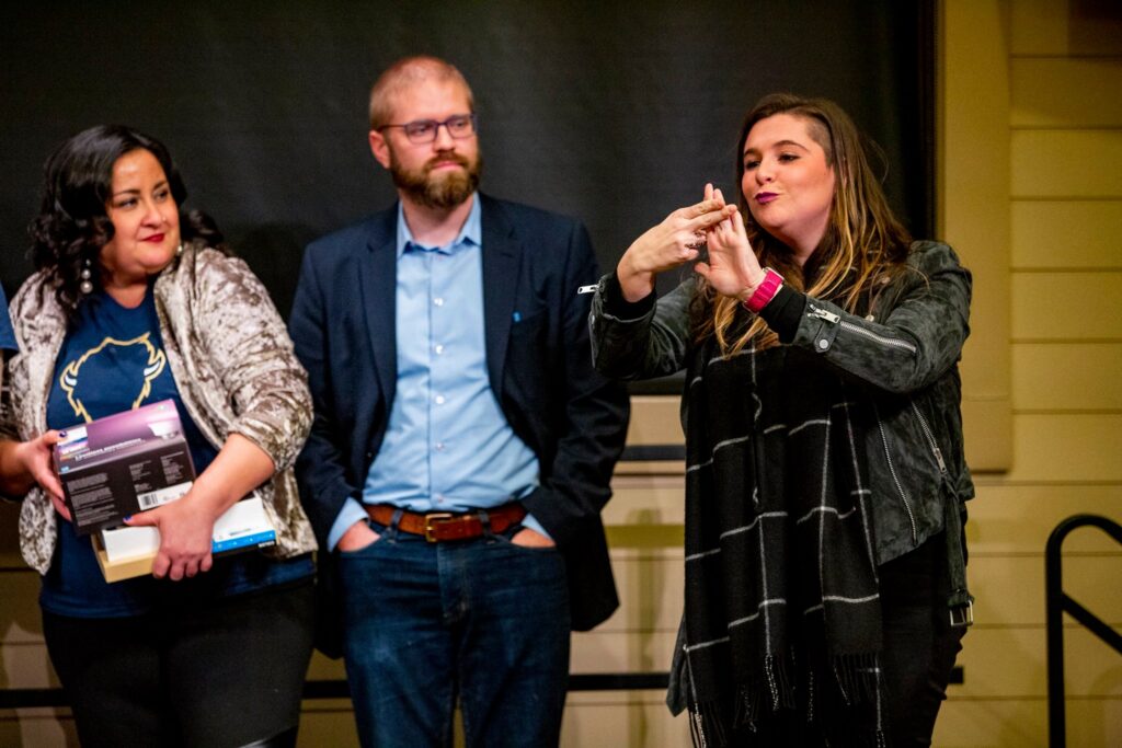 Michelle signing at a conference. Behind her onstage, a man and woman look on.