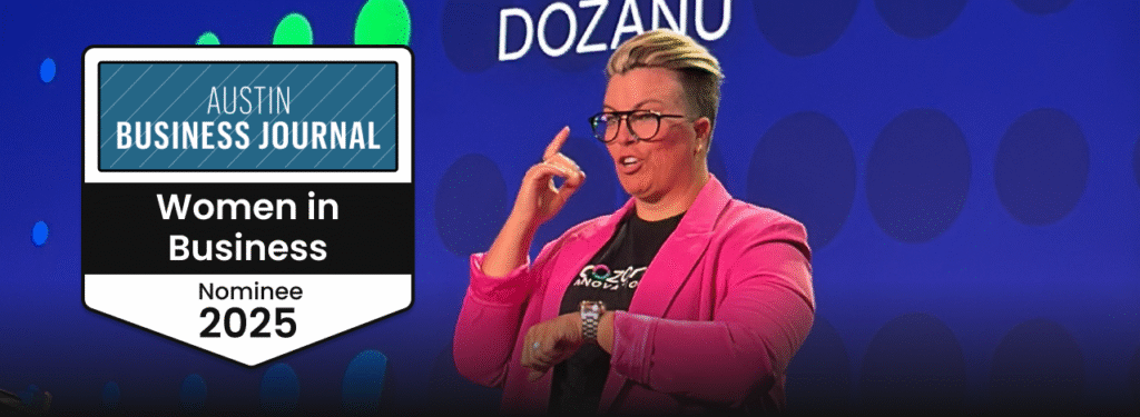 Katherine Lees, short blond hair, wearing a pink blazer and glasses, on stage at a conference. Next to her on the left, a banner displaying "Austin Business Journal Women in Business 2025."