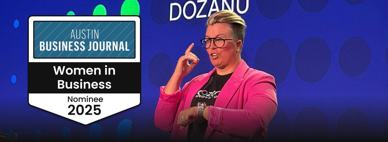 Katherine Lees, short blond hair, wearing a pink blazer and glasses, on stage at a conference. Next to her on the left, a banner displaying "Austin Business Journal Women in Business 2025."
